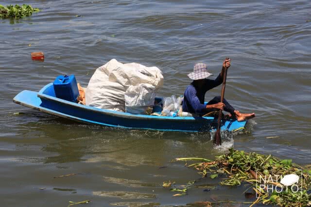 ชาวบ้านพายเรือเก็บขวดน้ำพลาสติกที่ลอยเกลื่อนในแม่น้ำ