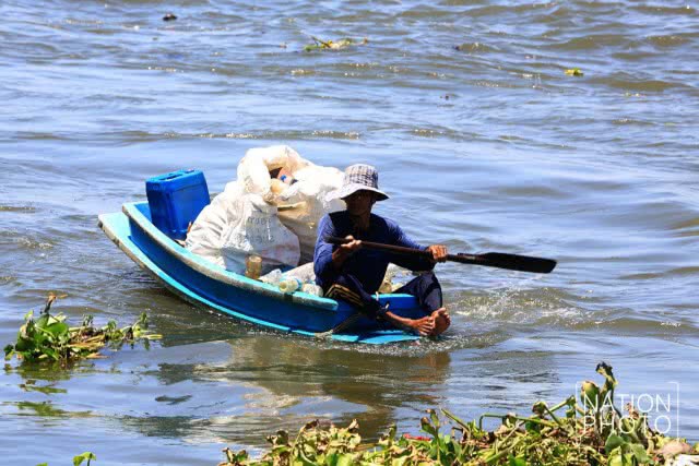 ชาวบ้านพายเรือเก็บขวดน้ำพลาสติกที่ลอยเกลื่อนในแม่น้ำ