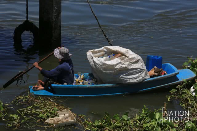 ชาวบ้านพายเรือเก็บขวดน้ำพลาสติกที่ลอยเกลื่อนในแม่น้ำ