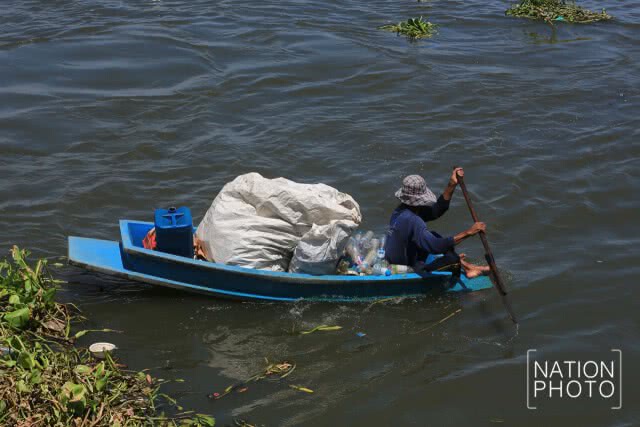 ชาวบ้านพายเรือเก็บขวดน้ำพลาสติกที่ลอยเกลื่อนในแม่น้ำ
