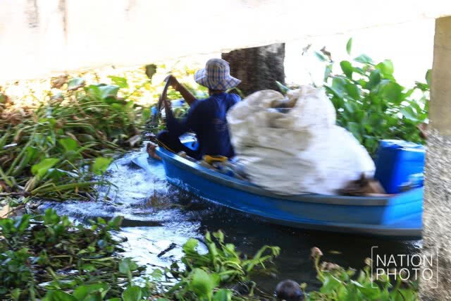 ชาวบ้านพายเรือเก็บขวดน้ำพลาสติกที่ลอยเกลื่อนในแม่น้ำ
